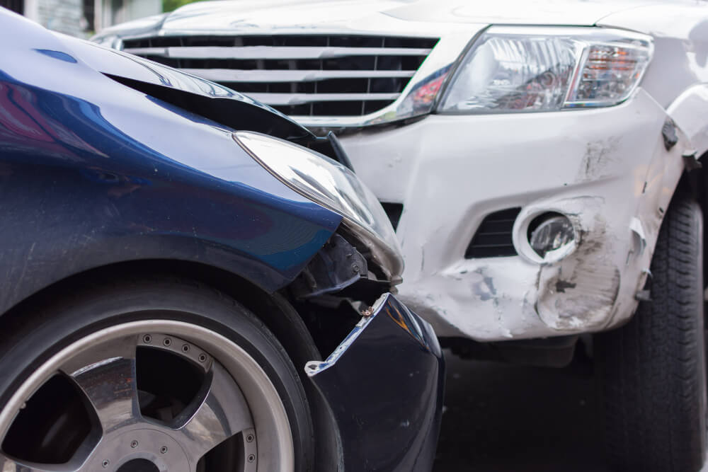 Ein blaues Auto und ein weißer SUV stehen nach einem Frontalzusammenstoß nah beieinander, beide Fahrzeuge sind sichtbar beschädigt