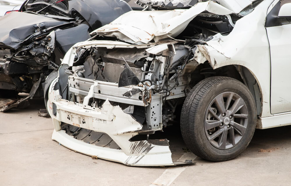 Ein weißes Auto mit stark beschädigter Front steht nach einem Unfall neben einem weiteren zerstörten Fahrzeug